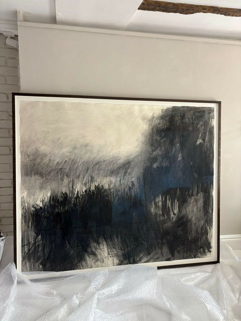 black and white charcoal drawing of abstracted landscape, mounted on white card and framed with thin brown wooden frame. sits on bubble wrap having just been unwrapped.The artwork is moody and atmospheric
