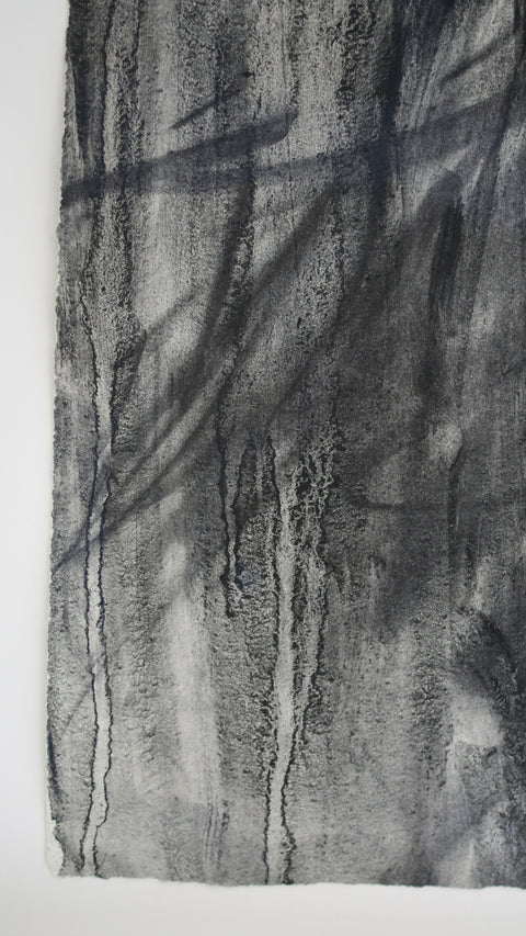 close up of charcoal marks and watery drips having run through the material on the surface of the paper. a decal edge is shown